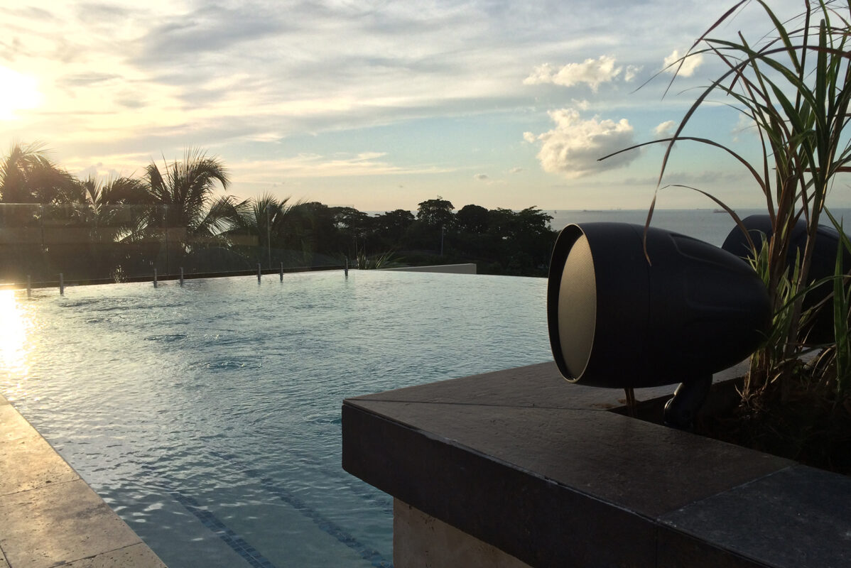 TruAudio landscape satellite speaker aimed across an infinity pool at golden hour